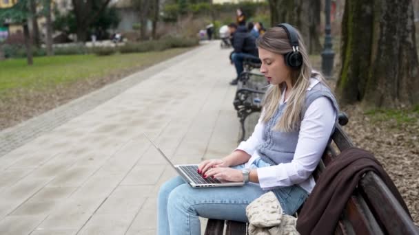 Молодая Деловая Женщина Сидит Парке Скамейке Работает Ноутбуке Слушая Музыку — стоковое видео