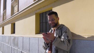 Şehir sokaklarının duvarına dayanan gözlüklü havalı elbiseli, genç, mutlu hippi adam sosyal ağda cep telefonu sohbeti yapıyor. Kentsel yaşam tarzı kavramı.