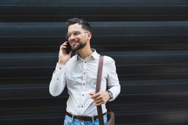 Ofis binasının önünde duran başarılı iş adamının portresi. Eğitimli bağımsız erkek takım lideri iş adamı siyah duvara karşı poz veriyor..
