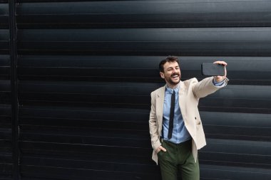 Ofis binasının önünde duran başarılı iş adamının portresi. Eğitimli bağımsız erkek takım lideri iş adamı siyah duvara karşı poz veriyor..