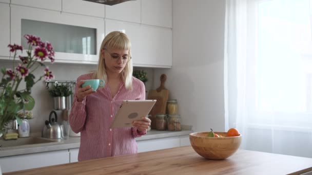 年轻的女商人 小公司业主 创业商人 营销和产品战略开发商 在厨房里用数字平板电脑看统计数字和邮件 喝第一杯咖啡 — 图库视频影像