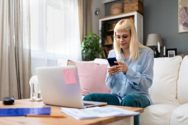 Genç iş kadını serbest olarak yurtdışında çalışıyor. Evde çalışırken akıllı telefon kullanarak iş görüşmesi için e-posta hazırlama, video görüntülü kamera ve dizüstü bilgisayardaki soruları kontrol ediyor.
