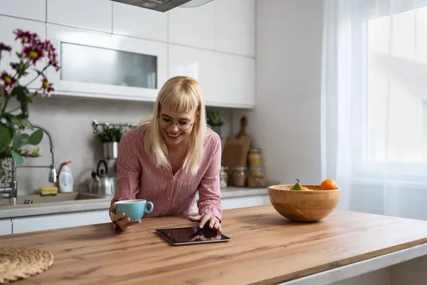 Young business woman, small company owner, startup businessperson expert marketing and product strategy developer, drinking first coffee in the kitchen using digital tablet to see statistics and mails