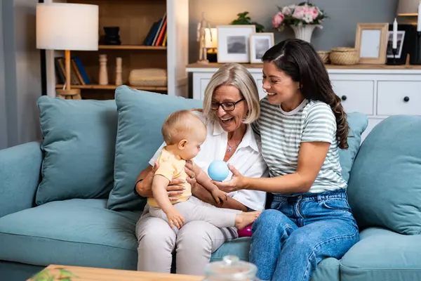 Three generational family together in their living room at home, relaxing with the grandmother. Grandmother and mother in living room with baby smiling. Multi-generation family portrait