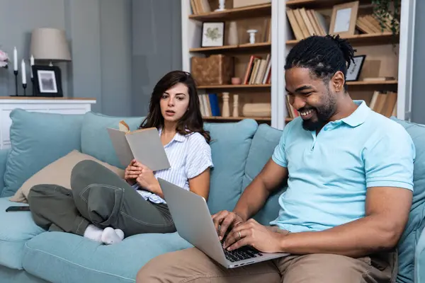 stock image Simple living. Young couple man and woman at home working on laptop, reading book, talking and argue, making fun. Real life situations of two people living together with support and issues