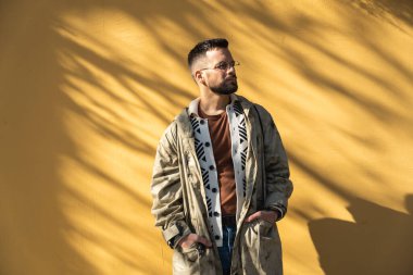 Sarı duvar arkaplanlı, dışarıda poz veren modaya uygun genç bir hippi. Tarz ve bağımsızlık bin yıllık erkek portre için ayakta duruyor. Dünya gezgini gençlik kültürü