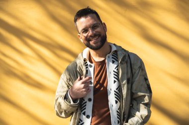 Sarı duvar arkaplanlı, dışarıda poz veren modaya uygun genç bir hippi. Tarz ve bağımsızlık bin yıllık erkek portre için ayakta duruyor. Dünya gezgini gençlik kültürü