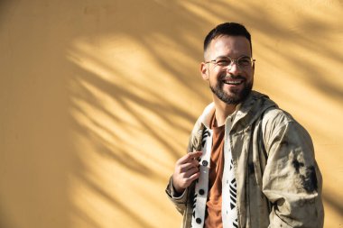 Sarı duvar arkaplanlı, dışarıda poz veren modaya uygun genç bir hippi. Tarz ve bağımsızlık bin yıllık erkek portre için ayakta duruyor. Dünya gezgini gençlik kültürü