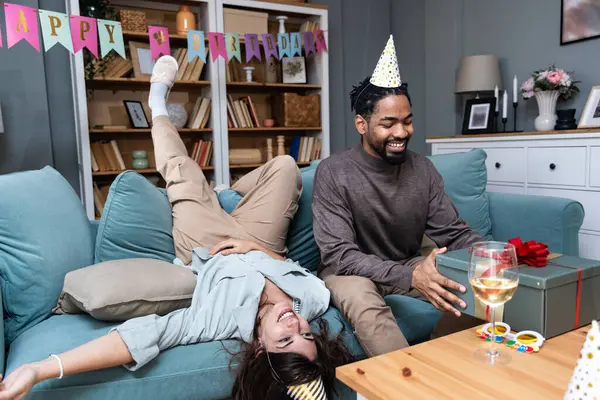 Crazy birthday party. Young couple celebrating birthday in their apartment alone having fun and joy with gift box as present. Making funny facial expression from happiness.