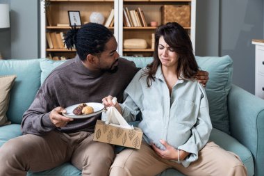 Evdeki oturma odasında kocasının yanında oturan hamile bir kadın ve hormonların değişmesi yüzünden üzgün ve üzgün hisseden bir çocuk babası. Hamilelik stresi sorunları
