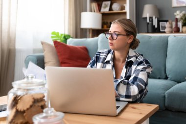 Genç hasta iş kadını evde çalışıyor, dizüstü bilgisayarla çalışıyor. Uzaktan kumandalı, şirketle kadın kablosuz bağlantısı, uzaktan finans ve ekonomi revizyonu. E-iş