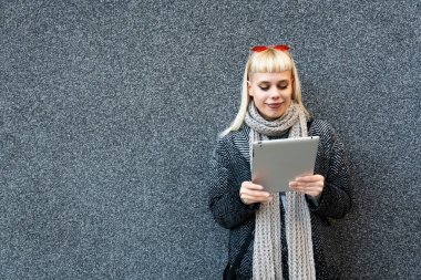 Ofis binasının dışında dijital tablet üzerinde çalışan havalı tavırlı, kendine güvenen, serbest çalışan genç bir kadının portresi. Hippi tarzı kadın siyah duvara poz veriyor..
