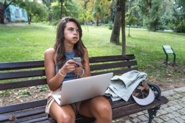 Milenyum çağında havalı davranışları olan genç bir hippi, yurtdışı değişim öğrencisi, parkta oturmuş dizüstü bilgisayarla çalışıyor. Uzaktan çalışma, online eğitim, e-ticaret telekomünikasyon.