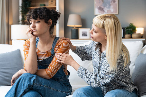 Young lesbian couple having relationship difficulties and arguing at home. Two women sitting on sofa, not talking after argue, feeling depressed and insulted, not talking.