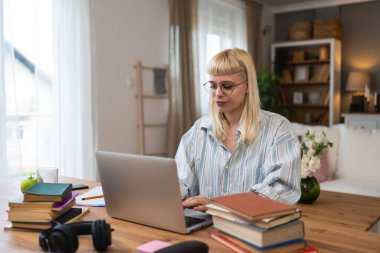 Kişisel gelişim. Genç, memnun öğrenci ya da iş kadını, bilgisayarla evden çalışıyor, kitaplardan öğreniyor, iş alanında yenilikler yapıyor ya da eğitim sınavlarına hazırlanıyor..