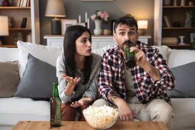 Genç çift, erkek ve kadın, kanepede oturuyor, bira içiyor, patlamış mısır yiyor ve korku filmi izliyor ya da dramatik aksiyon ya da dramatik film izliyor. Basit yaşam konsepti, hafta sonu aktiviteleri.