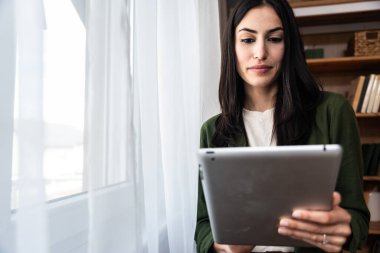 Ev ofisinde dijital tablet üzerinde çalışan çekici bir kadın. İş kadını küçük bir şirket sahibi dairesinden internet üzerinden çalışıyor. Bağımsız serbest grafik tasarımcı kadın özgürlük ve işin tadını çıkarıyor.