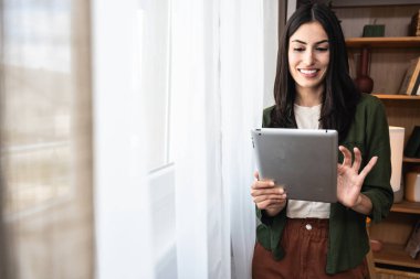 Ev ofisinde dijital tablet üzerinde çalışan çekici bir kadın. İş kadını küçük bir şirket sahibi dairesinden internet üzerinden çalışıyor. Bağımsız serbest grafik tasarımcı kadın özgürlük ve işin tadını çıkarıyor.