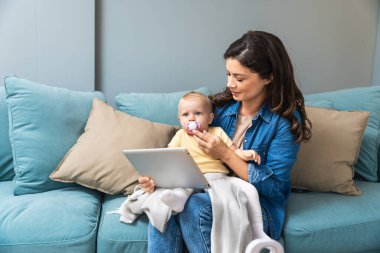 Mutlu aile anne ve çocuk kızı dijital tablet kanepe, oturma kullanma pc bilgisayar ekranına bakarak tutan kız çocuk ile üst annesi gülümseyerek görüntülü görüşme saat karikatürler online alışveriş yapmak yapmak