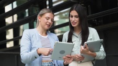 İki genç iş kadını tasarımcı ofis çalışanı, gurbetçi küresel iş mesleği, pazarlama ve finans uzmanları, ofis binasının dışında duran dijital tablete bakıyor,