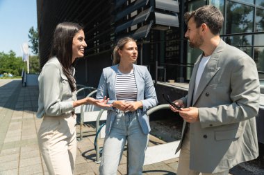 Bir grup başarılı iş adamı, işadamı ve iş kadını resmi giysiler içinde ofis binasının önünde durmuş iş hakkında tartışıyorlar. Harika mutlu gurbetçi şirket uzmanları bilgi alışverişinde bulunuyor.