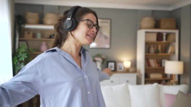 Kulaklık takan mutlu bir milenyum kızı müzik dinleyerek eğleniyor oturma odasında dinleniyor, kulaklıklı mutlu genç bir kadın dans ediyor evde hafta sonunun keyfini çıkarıyor, stresten uzak bir konsept.