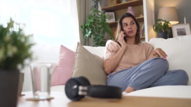 Telefon görüşmesi. Kendine güvenen genç bir kadın kanepeye oturur ve konuşur. Kulağında bir cihazla telefonla konuşur. Cep telefonuyla cevap veren kadın arkadaş ebeveyni dinliyor..