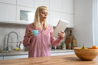 Genç iş kadını emlakçı sabah rutini, mutfakta kahve içmek e-postaları okumak için dijital tablet kullanmak. Evde çalışan kadın profesyonel tasarımcı, iş sahibi, kendine güvenen bir yaşam tarzı var.