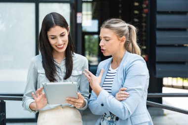 Dijital tablet kullanan ve dışarıda dikilen iki iş arkadaşı. Modern iş arkadaşları işe giderken ofis binasının önünde sohbet ediyorlar. İş adamları işbirliği.