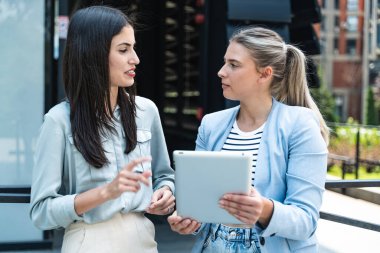 Dijital tablet kullanan ve dışarıda dikilen iki iş arkadaşı. Modern iş arkadaşları işe giderken ofis binasının önünde sohbet ediyorlar. İş adamları işbirliği.