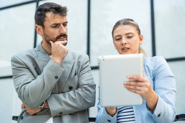 Two coworkers using a digital tablet and talking while standing outside. Modern business colleagues chatting together in front of office building on their way to work. Businesspeople collaboration clipart