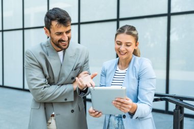 Dijital tablet kullanan ve dışarıda dikilen iki iş arkadaşı. Modern iş arkadaşları işe giderken ofis binasının önünde sohbet ediyorlar. İş adamları işbirliği.