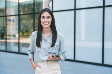 Dijital tabletle ofis binasının önünde duran genç iş kadını takım lideri. Finansal bölgedeki iş yerinin dışında başarılı bir tasarımcının portresi. İş insanları