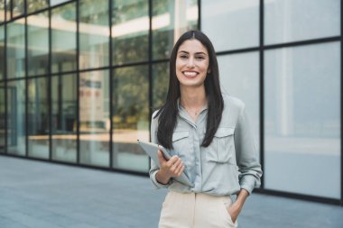 Dijital tabletle ofis binasının önünde duran genç iş kadını takım lideri. Finansal bölgedeki iş yerinin dışında başarılı bir tasarımcının portresi. İş insanları