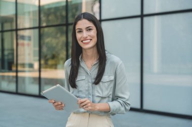 Dijital tabletle ofis binasının önünde duran genç iş kadını takım lideri. Finansal bölgedeki iş yerinin dışında başarılı bir tasarımcının portresi. İş insanları