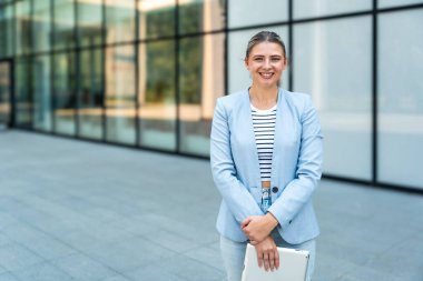 Dijital tabletle ofis binasının önünde duran genç iş kadını takım lideri. Finansal bölgedeki iş yerinin dışında başarılı bir tasarımcının portresi. İş insanları