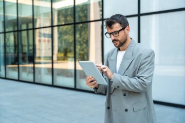 Dijital tabletle ofis binasının önünde duran genç bir iş adamı takım lideri. Finansal bölgedeki iş yerinin dışında başarılı bir tasarımcının portresi. İş insanları