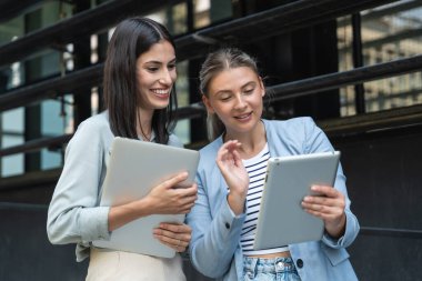 İki iş kadını bilgisayar ve dijital tabletle ofis binası dışında. Modern iş hayatında kullanılan teknoloji. Sürdürülebilir enerji uzmanları, geliştiriciler ve tasarım uzmanları birlikte çalışıyorlar.