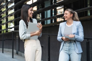 İki iş kadını bilgisayar ve dijital tabletle ofis binası dışında. Modern iş hayatında kullanılan teknoloji. Sürdürülebilir enerji uzmanları, geliştiriciler ve tasarım uzmanları birlikte çalışıyorlar.