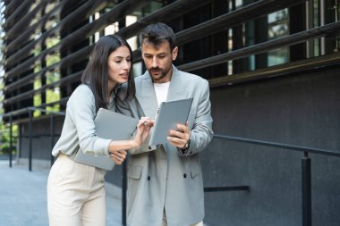 İş adamı ve kadın bilgisayar ve dijital tabletle ofis binası dışında. Modern iş hayatında kullanılan teknoloji. Sürdürülebilir enerji uzmanları geliştiriciler ve tasarım profesyonelleri birlikte çalışıyorlar.