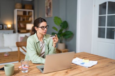 Genç iş kadını ev ekonomisi ya da internet alışverişini kredi kartı ve dizüstü bilgisayarla yapmak için ev işlerinde çalışmaya ara veriyor. Kendine güvenen bir kadın internetten sipariş veriyor..