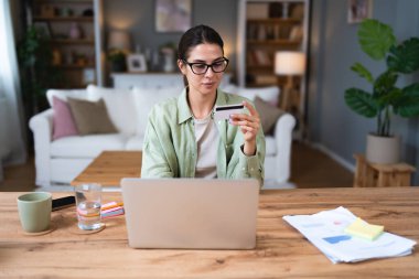 Genç iş kadını ev ekonomisi ya da internet alışverişini kredi kartı ve dizüstü bilgisayarla yapmak için ev işlerinde çalışmaya ara veriyor. Kendine güvenen bir kadın internetten sipariş veriyor..