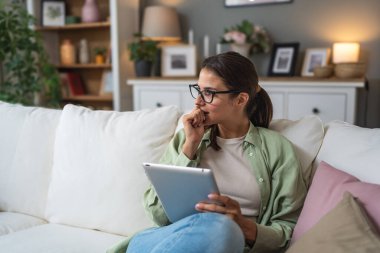 Çekici kadın, serbest çalışan, dijital tablet kullanan, oturma odasındaki rahat koltukta oturan. Başarılı bir iş kadını evde mesaj atıyor. Çevrimiçi teknoloji konsepti, uzak iş ve çalışma.