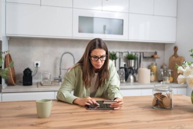 Kafası karışmış genç bir kadın elinde dijital tablet ekranına bakarken online bankacılık veya alışveriş, kredi kartı limiti ve aşırı harcama sorunları yaşıyor.
