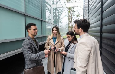 Bir grup başarılı iş adamı ofis binasının önünde durmuş fırsatları tartışıyor ve çalışanların kurumsal personel toplantısına hazırlanıyor..