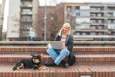 Young adult woman or girl, college university student, exchange student, freelancer or expatriate working on laptop outdoor with her adopted or rescued pet dog. Business work outside, freedom concept clipart