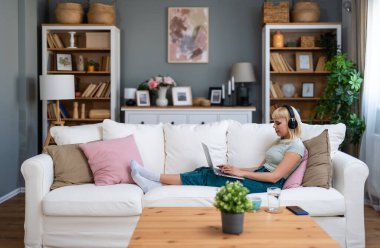 Genç, mutlu, serbest çalışan bir işçi ya da üniversiteli bir kadın evinde oturmuş dizüstü bilgisayarla çalışıyor, podcast dinliyor ya da en sevdiği şarkıyı dinliyor, özgürlüğün ve bağımsızlığın tadını çıkarıyor..