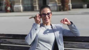 Genç bayan profesyonel iş adamı akıllı telefondan sesli mesaj dinliyor. İş kadını bankta oturuyor cep telefonundan gelen postaları dinliyor, işyerinden iyi haberler alıyor..