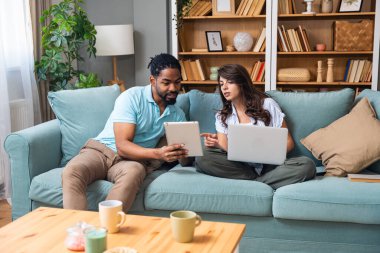 Evde dizüstü bilgisayarda ve yeni projede dijital tablette çalışan genç çift. Yenilikçi teknoloji uzmanları çevrimiçi çalışmalarla finans ve ekonomi krizine çözüm buldular.
