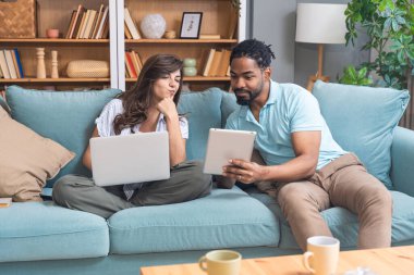 Evde dizüstü bilgisayarda ve yeni projede dijital tablette çalışan genç çift. Yenilikçi teknoloji uzmanları çevrimiçi çalışmalarla finans ve ekonomi krizine çözüm buldular.